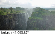 The flows of the Zambezi River collapse from the edge of the plateau. Fog over steep rocky slopes. Lush tropical vegetation all around. Cloudy sky. Victoria Falls. Zimbabwe (2020 год). Стоковое фото, фотограф Вера Ивановна Кубарева / Фотобанк Лори