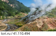 Columns of steam from hot springs rise above the hillside. The river winds along a rocky bed. Green mountains against a blue sky. Kamchatka. Valley of Geysers. Стоковое фото, фотограф Вера Ивановна Кубарева / Фотобанк Лори