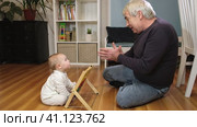 Grandfather playing with little baby. Caring granddad and cute toddler grandchild lying on warm floor together, having fun at home. Happy old senior man teach little grandson playing colorful blocks. Стоковое видео, видеограф Марина Демидюк / Фотобанк Лори