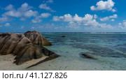 Picturesque granite boulders on the sandy beach of a tropical island. The turquoise ocean is washed by unusual stones with smoothed folded slopes. Blue sky, clouds. Seychelles. La Digue. Стоковое фото, фотограф Вера Ивановна Кубарева / Фотобанк Лори
