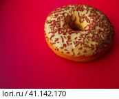 A doughnut or donut. A type of leavened fried dough. Sweet snack that can be homemade or purchased in bakeries, supermarkets, food stalls. Delicious pie with light icing on a red background. Стоковое фото, фотограф Юлия Петровская / Фотобанк Лори