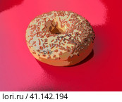 A doughnut or donut. A type of leavened fried dough. Sweet snack that can be homemade or purchased in bakeries, supermarkets, food stalls. Delicious pie with light icing on a red background, illusion. Стоковая иллюстрация, иллюстратор Юлия Петровская / Фотобанк Лори