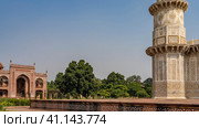 The ancient complex tomb of Itmad-Ud-Daulah. Marble corner minaret with ornaments, inlays of precious stones against the blue sky. In the distance is a red sandstone building with arches. India. Agra (2022 год). Стоковое фото, фотограф Вера Ивановна Кубарева / Фотобанк Лори