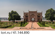 The building in the complex of the tomb of Itmad-Ud-Daula, built of red sandstone, by the river. Arches, spires, white ornaments are visible. Green vegetation on the sides of paved footpaths. India. (2022 год). Стоковое фото, фотограф Вера Ивановна Кубарева / Фотобанк Лори