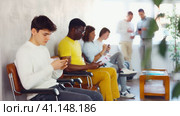 Serious man browsing websites on smartphone while sitting in lobby of job center or employment office, waiting for interview or conversation with career counselor. Стоковое видео, видеограф Яков Филимонов / Фотобанк Лори