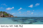 Picturesque granite boulders with smoothed outlines pile up at the edge of the ocean on the beach. Clear turquoise water. Green hill on the background of azure sky and clouds. Seychelles. La Digue. Стоковое фото, фотограф Вера Ивановна Кубарева / Фотобанк Лори