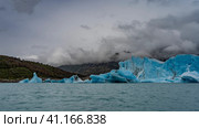 Amazing blue glacier in turquoise lake. A wall of cracked ice, broken icebergs in the water. Coastal mountains in clouds and fog. Perito Moreno glacier. Los Glaciares National Park. Argentina. El Calafate. Стоковое фото, фотограф Вера Ивановна Кубарева / Фотобанк Лори