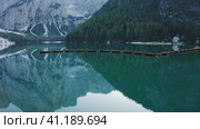 Most beautiful Lago di Braies also known Pragser Wildsee. Dolomites, Italy. Flying out over the calm emerald green water surface and boats in a raw. Стоковое фото, фотограф Igor Tichonow / Фотобанк Лори
