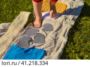 Children's feet walk on an orthopedic massage diy mat with surfaces of various shapes and tactility. grass, cones, acorns - texture details. Prevention and treatment of flat feet. Стоковое фото, фотограф Ирина Старикова / Фотобанк Лори