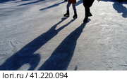Children ride in a city park on an ice rink. Feet skater while skating on ice. The low winter sun weakly illuminates the ice. Dark shapes and long shadows on the surface. Sports movements. Стоковое фото, фотограф Юлия Петровская / Фотобанк Лори