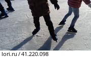Children ride in a city park on an ice rink. Feet skater while skating on ice. The low winter sun weakly illuminates the ice. Dark shapes and long shadows on the surface. Sports movements. Стоковое фото, фотограф Юлия Петровская / Фотобанк Лори