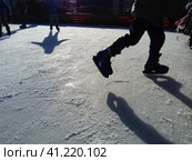 Children ride in a city park on an ice rink. Feet skater while skating on ice. The low winter sun weakly illuminates the ice. Dark shapes and long shadows on the surface. Sports movements. Стоковое фото, фотограф Юлия Петровская / Фотобанк Лори