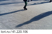 Children ride in a city park on an ice rink. Feet skater while skating on ice. The low winter sun weakly illuminates the ice. Dark shapes and long shadows on the surface. Sports movements. Стоковое фото, фотограф Юлия Петровская / Фотобанк Лори