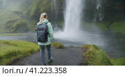 Woman with backpack walking towards Seljalandsfoss waterfall Iceland. Стоковое видео, видеограф Igor Tichonow / Фотобанк Лори