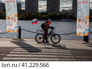 Мужчина стоит с велосипедом на набережной Северного Речного вокзала в солнечный день во время проведения Московского осеннего велофестиваля в городе Москве, Россия (2023 год). Редакционное фото, фотограф Николай Винокуров / Фотобанк Лори