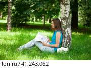 Happy woman leafing through a magazine while sitting in the summer park. Стоковое фото, фотограф Андрей Аркуша / Фотобанк Лори