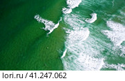 Aerial view of waves of emerald green ocean rolling towards the shore. Unrecognized surfer trying to. Стоковое видео, видеограф Igor Tichonow / Фотобанк Лори