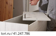 A man collects a bookcase. It fixes with screws the loops on the door from the cabinet. Uses a screwdriver. Close-up.. Стоковое видео, видеограф Vadzim Yakubovich / Фотобанк Лори