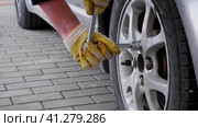 A man wearing protective gloves tightens the wheel nuts with a wrench. Change of seasonal tires. Стоковое видео, видеограф Алексей Гекало / Фотобанк Лори