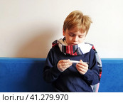 The boy got sick, his throat hurts and his body temperature rises. The childs neck is wrapped in a warm scarf. The kid looks dejectedly at the thermometer and is surprised. Стоковое фото, фотограф Юлия Петровская / Фотобанк Лори