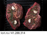 Two raw ribeye steaks with spices, rosemary and garlic on a grill pan. Стоковое фото, фотограф Максим Коломыченко / Фотобанк Лори