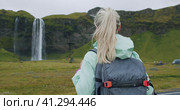 Close up of Woman with backpack enjoying famous Seljalandsfoss waterfall Iceland. Стоковое видео, видеограф Igor Tichonow / Фотобанк Лори
