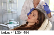 Skilled female dermatologist performing cosmetic scalp injections of steroids to brown-haired young woman to stimulate follicles and improve hair growth and density. Стоковое видео, видеограф Яков Филимонов / Фотобанк Лори