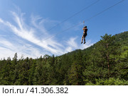Girl tourist is going down the ropes - a bungee cable - from a mountain waterfall above the wooded gorge of the Kyngarga River. Extremely active summer holiday. Siberia. Buryatia. Arshan resort. Стоковое фото, фотограф Виктория Катьянова / Фотобанк Лори