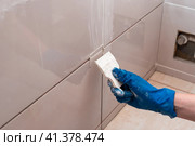 Repair and wall cladding with tiles. The master rubbing the tile joints with a white putty with a rubber spatula. Стоковое фото, фотограф Коханова Наталья / Фотобанк Лори