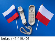 Старый телефон и два флага на синем фоне, концепция на тему телефонных переговоров между Польшей и Россией. Стоковое фото, фотограф Сергей Чайко / Фотобанк Лори
