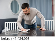 Young bachelor wiping surface of dining table in apartment. Стоковое фото, фотограф Яков Филимонов / Фотобанк Лори