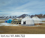 Mongolian yurt camp in the winter steppe. An old truck stands next to the yurts against the backdrop of snow-capped mountains. Стоковое фото, фотограф Саблин Станислав / Фотобанк Лори