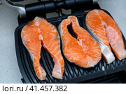 Three raw salmon steaks are toasted on a modern electric non-stick coating grill. Healthy eating concept. Close up photo with selective focus. Три стейка из сырого лосося поджариваются на современном электрическом гриле с антипригарным покрытием. Концепция здорового питания. Фотография крупным планом с выборочным фокусом. Стоковое фото, фотограф Дмитрий Березнев / Фотобанк Лори