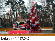 Balashikha, Russia - January 18, 2020. New Year's decorations in Pekhorka park. Artificial red pine tree and red old timer GAZ-M20 Pobeda delivering gifts. Редакционное фото, фотограф Александр Кузнецов / Фотобанк Лори