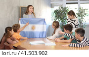 Group of curious preteen learners and young female teacher with flag of Argentina in classroom of academy. Стоковое видео, видеограф Яков Филимонов / Фотобанк Лори