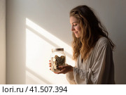 Young woman holding in her hands a jar of coins on light background with copy space. Money, finance, savings concept. AI generated. Стоковое AI-изображение, AI-художник Александра Селина / Фотобанк Лори