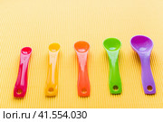 Мерные ложки на желтом фоне. Разноцветные пластиковые мерные ложки. Measuring spoons on a yellow background. Multi-colored plastic measuring spoons. Стоковое фото, фотограф Ольга Митряева / Фотобанк Лори