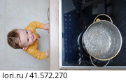 Toddler baby boy looks at a pot of boiling water. Child safety issues in the home room, little kid. Стоковое фото, фотограф Андрей Журавлев / Фотобанк Лори