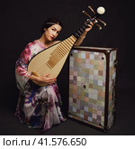 A happy female musician in Asian clothes on a studio black background. A smiling woman with a stringed musical instrument from Asia on a dark background. Стоковое фото, фотограф Андрей Журавлев / Фотобанк Лори