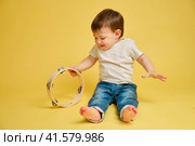 Toddler baby plays the tambourine, a child with a percussion musical instrument on a studio yellow background. Happy child musician playing hand drum. Kid aged one year four months. Стоковое фото, фотограф Андрей Журавлев / Фотобанк Лори