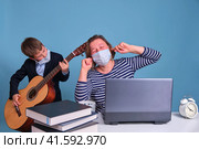 The son with the guitar prevents his mother from working remotely at the computer at a distance. Problems working remotely during a lockdown. Стоковое фото, фотограф Андрей Журавлев / Фотобанк Лори