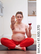 Fitness during pregnancy and abstinence from drinking wine. A pregnant woman at a sports training session at home shows a stop gesture as a sign of giving up alcohol. Стоковое фото, фотограф Андрей Журавлев / Фотобанк Лори