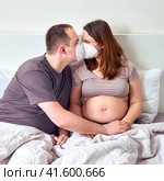 A man and a pregnant woman kiss in medical masks n95 ffp2. Coronavirus problems and excessive protection. Стоковое фото, фотограф Андрей Журавлев / Фотобанк Лори