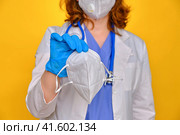 Doctor with a medical mask n95 ffp2 in his hand, closeup. Nurse gives face masks on a yellow background. Coronavirus pandemic protective clothing concept. Стоковое фото, фотограф Андрей Журавлев / Фотобанк Лори