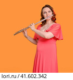 Portrait of a woman musician with a flute on a studio yellow background. Flutist with a large concert transverse flute in her hands. Стоковое фото, фотограф Андрей Журавлев / Фотобанк Лори