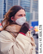 Woman with curly hair in a medical mask ffp2 respirator against the background of urban houses, outdoor. Стоковое фото, фотограф Андрей Журавлев / Фотобанк Лори