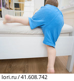 The baby is climbing on a high bed, risking an indoor accident. Kid aged two years (two-year-old boy) Стоковое фото, фотограф Андрей Журавлев / Фотобанк Лори