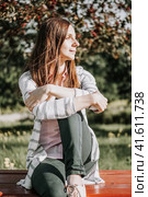 Portrait of a young woman who sits on a bench. the head is turned towards the sun. The girl in casual wear enjoys the beautiful weather. Walk outdoors concept. Стоковое фото, фотограф Константин Григорьев / Фотобанк Лори