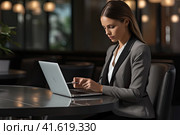 A young beautiful businesswoman is sitting at a table in front of a laptop and looking at the screen. Generated by AI. Стоковое AI-изображение, AI-художник Ярославский Максим / Фотобанк Лори