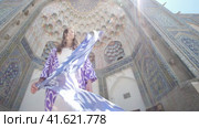 A young woman with long hair in an oriental robe and a skullcap walks through an ancient oriental city. Стоковое видео, видеограф Aleksey Kidisyuk / Фотобанк Лори